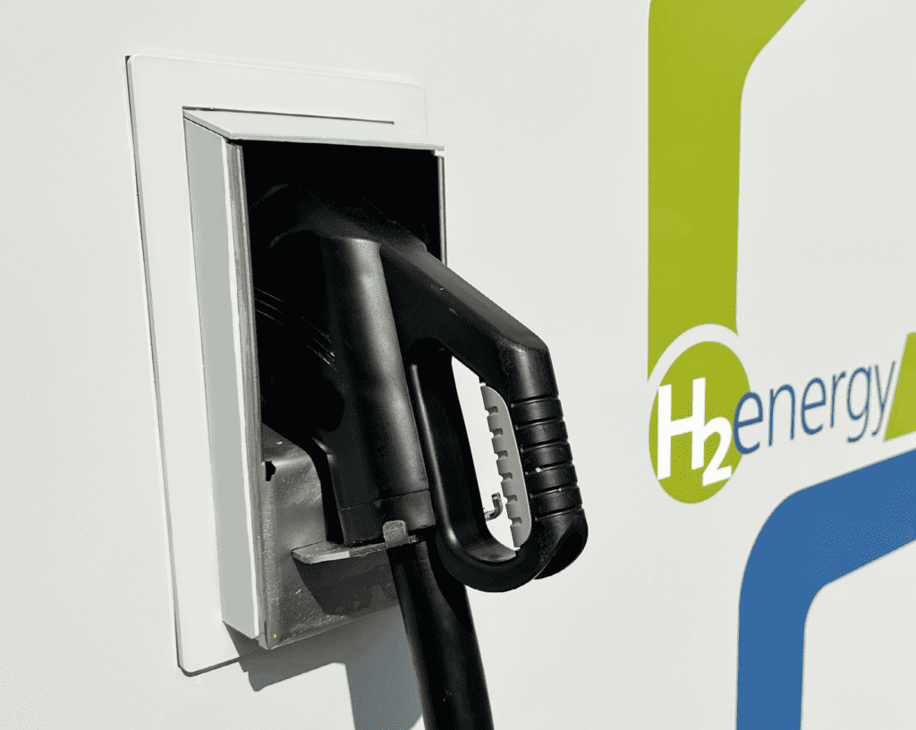 A hydrogen fuel pump nozzle is docked in its holder beside a sign that reads “H2 energy.”.