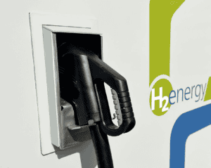 A hydrogen fuel pump nozzle is docked in its holder beside a sign that reads “H2 energy.”.